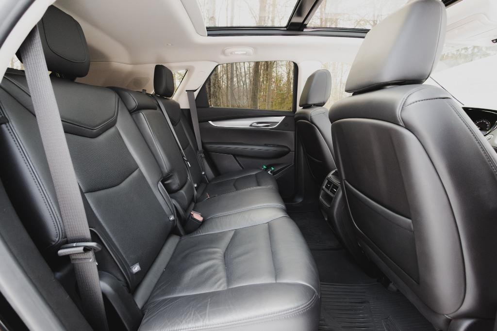 Cadillac XT5 interior — black leather rear bench seating with panoramic sunroof and wooded view
